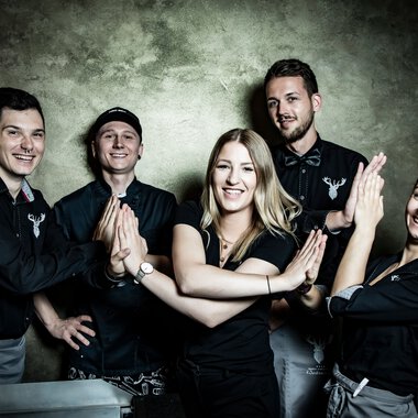 Fünf Mitarbeiter des Service-Teams Walserhof bei Werner Krug, posieren lachend vor einem Wand hinter ihnen. | © Kleinwalsertal Tourismus eGen • Fotograf: Werner Krug